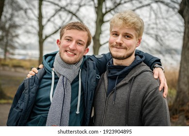 A Healthy Blonde Man Living With HIV Standing With His Arm Around His Friend At A Park In Hamburg, Germany