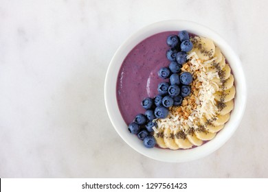 Healthy blueberry smoothie bowl with coconut, bananas, chia seeds and granola. Top view on a bright background.