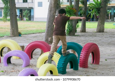 Healthy Boy playing alone in the playground in the shool by jumping on the decorate colorfull tyres