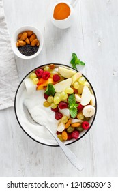 Healthy breakfast bowl: natural yogurt and fruits (grapes, apple, raspberry, mint, peach, banana) on white wooden table top view