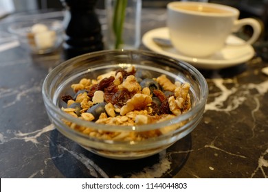 Healthy breakfast bowl of nuts, grains, berries, blueberries, yoghurt and raisins on a table with coffee in the background