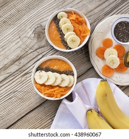 Healthy breakfast. Carrot Banana smoothie with granola and chia seeds on a simple wooden background in portioned cups decorated with slices of vegetables and fruits. selective focus