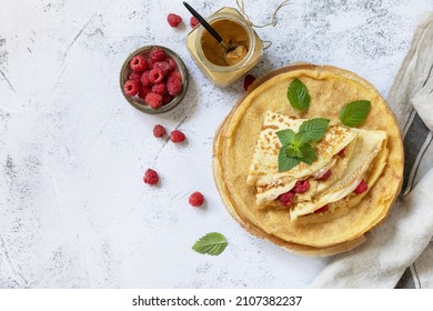 Healthy breakfast, celebrating Pancake day. Delicious homemade crepes with rasberries and peanut paste on a stone tabletop. Top view flat lay. Copy space.