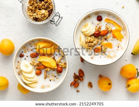 Healthy breakfast cereal top view. Granola breakfast with fruits, nuts, milk and peanut butter in bowl on a white background
