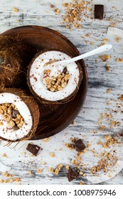 Healthy Breakfast In Coconut Bow On White Background. Yogurt In Coconut Bowl With Coconut Flakes, Chocolate And Granola. Top View, Flat Lay, Overhead