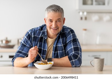 Healthy breakfast concept. Cheerful senior man having breakfast, eating cereals and drinking coffee, sitting in kitchen interior and enjoying morning time on weekend, free space - Powered by Shutterstock