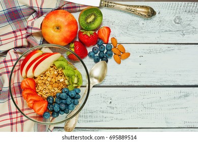 Healthy breakfast concept - multigrain granola with apple, kiwi, almonds, strawberry and blueberry - top view in rural style on wooden table with vintage knife and checkered textile - Shutterstock ID 695889514