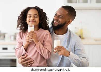 Healthy Breakfast. Cute Little African American Girl And Her Handsome Bearded Dad Drinking Milk From Glasses In Kitchen. Father Embracing And Looking At His Happy Daughter. Time For Vitamins