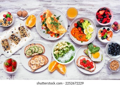 Healthy breakfast food table scene. Above view over a white wood background. Omelette, nutritious bowl, toasts, granola bars, smoothie bowl, yogurts and fruits. - Powered by Shutterstock