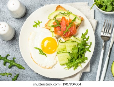 Healthy Breakfast. Fried Egg, Toast With Salmon And Avocado And Fresh Salad. Top View With Copy Space At Kitchen Table.