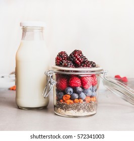  Healthy breakfast in glass making with oatmeal , Chia seeds, Goji berries, fresh berries and bottle of milk  , front view, close up