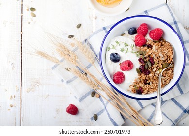 Healthy breakfast. Granola, muesli with pumpkin seeds, honey, yogurt and fresh berries in a ceramic bowl  with a cup of coffee on white background. 