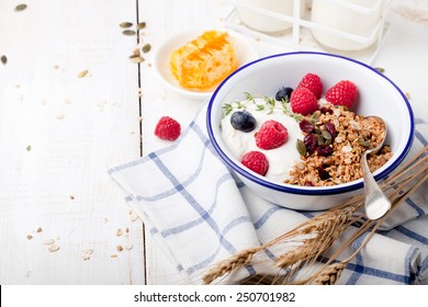 Healthy breakfast. Granola, muesli with pumpkin seeds, honey, yogurt and fresh berries in a ceramic bowl  with a cup of coffee on white background. 