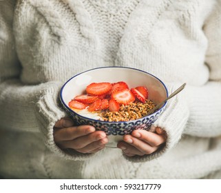 Healthy Breakfast Greek Yogurt, Granola And Strawberry Bowl In Hands Of Woman Wearing White Loose Woolen Sweater, Selective Focus. Clean Eating, Healthy, Vegetarian, Dieting Food Concept