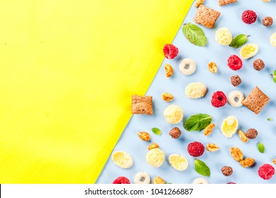 Healthy breakfast ingredients concept. Various breakfast cereal, raspberries and mint on blue yellow background, copy space top view
