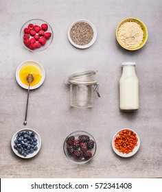 Healthy breakfast  ingredients : honey, oatmeal , Chia seeds, Goji berries, fresh berries and bottle of milk  with empty glass on gray background, top view, flat lay