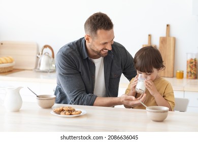 Healthy breakfast for kids. Positive loving father giving glass of fresh milk to his little son, asirabble boy enjoying tasty drink, sitting together at home kitchen - Powered by Shutterstock