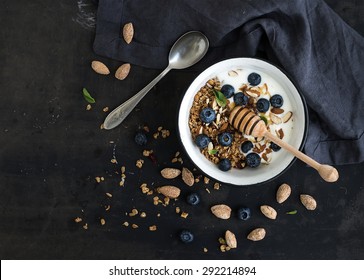 Healthy breakfast. Oat granola with fresh blueberries, almond, yogurt and mint in a rustic metal bowl over dark grunge surface. Top view, copy space - Powered by Shutterstock