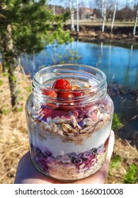 Healthy Breakfast Overnight Oats With Strawberries, Blueberries And Yoghurt In A Glass Jar With Beautiful Outdoor Background - Trees, Grass And Water. Food Prep And Meal Prep Concept