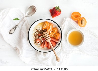 Healthy breakfast set. Rice cereal or porridge with fresh strawberry, apricots, almond and honey over white rustic wood backdrop, top view - Powered by Shutterstock