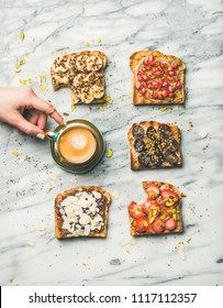 Healthy Breakfast, Snack. Flat-lay Of Vegan Wholegrain Toasts With Fruit, Seeds, Nuts, Peanut Butter And Woman's Hand Taking Cup Of Espresso Over Marble Background, Top View. Clean Eating Food Concept