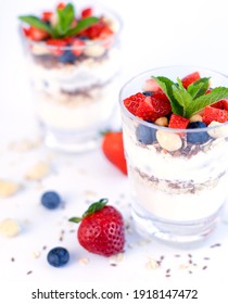 Healthy breakfast of strawberry parfait made with fresh fruit, yogurt, blueberries, flax seeds and muesli, white background. Small depth of field with selective focus on the glass jar in front