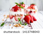 Healthy breakfast of strawberry parfaits made with fresh fruit, yogurt and granola over a rustic white table. Shallow depth of field with selective focus on glass jar in front. Blurred background.
