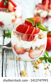 Healthy breakfast of strawberry parfaits made with fresh fruit, yogurt and granola over a rustic white table. Shallow depth of field with selective focus on glass jar in front. Blurred background. - Shutterstock ID 1413747995