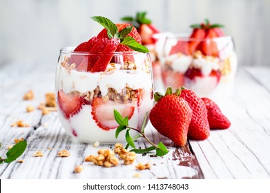 Healthy breakfast of strawberry parfaits made with fresh fruit, yogurt and granola over a rustic white table. Shallow depth of field with selective focus on glass jar in front. Blurred background. - Shutterstock ID 1413748043