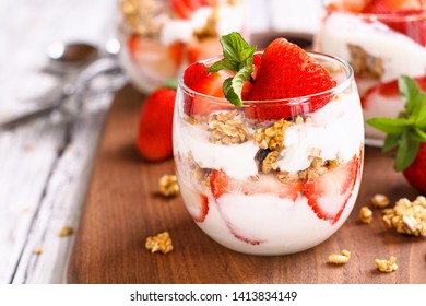 Healthy breakfast of strawberry parfaits made with fresh fruit, yogurt and granola over a rustic white table. Shallow depth of field with selective focus on glass jar in front. Blurred background. - Shutterstock ID 1413834149