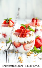 Healthy breakfast of strawberry parfaits made with fresh fruit, yogurt and granola over a rustic white table. Shallow depth of field with selective focus on glass jar in front. Blurred background. - Shutterstock ID 1413847925