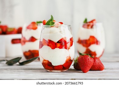 Healthy breakfast of strawberry parfaits made with fresh fruit, and yogurt over a rustic white table. Selective focus on glass jar in front. Blurred background and foreground.