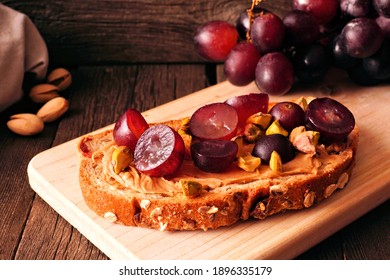 Healthy Breakfast Toast With Nut Butter, Grapes And Pistachios On Multi Grain Bread. Close Up On A Dark Wood Background.