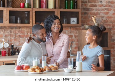 Healthy Breakfast Together. Cheerful African Family Drinking Milk And Eating Sweets At Kitchen, Copy Space