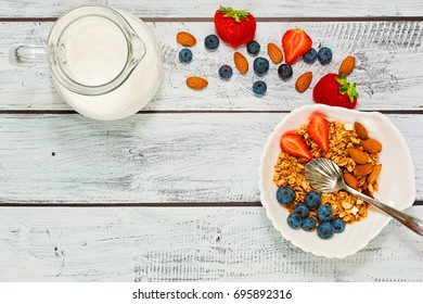 Healthy breakfast in top view - multigrain cereals with strawberry and blueberry, apple and almonds, pot with milk in flat lay on wooden table in rural style. - Shutterstock ID 695892316