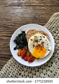 Healthy Breakfast - Wholemeal Bread, Fried Egg, Caramelized Tomatoes And Spinach With Garlic Isolated On Wooden Table And Knitted Table Cloth. Flatlay And Top View