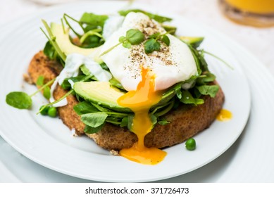 Healthy Breakfast with Wholemeal Bread Toast and Poached Egg with Green Salad, Avocado and Peas. Orange Juice and Orange Slices on the Background. - Shutterstock ID 371726473