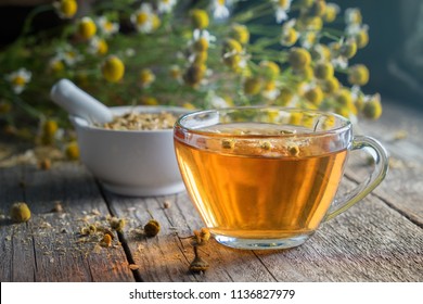 Healthy chamomile tea or infusion, mortar and daisy herbs on wooden table.