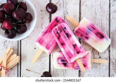 Healthy cherry yogurt popsicles. Top view table scene over a rustic white wood background.