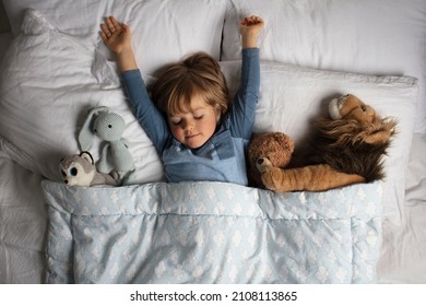 Healthy child, sweetest blonde toddler boy sleeping in a bed with a teddy bear and another stuffed animals. Beautiful baby boy have a healthy sleep in the bed. Sleeping baby. - Powered by Shutterstock