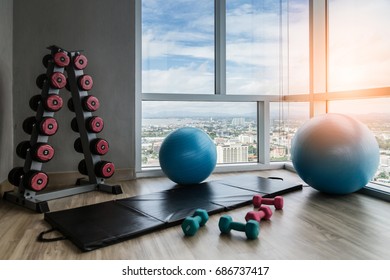 Healthy Concept With Fitness Center Dumbell Rack And Yoga Ball With Exercise Mat On Wooden Floor With Background Of Blue Sky