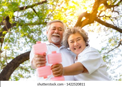 Healthy Concept. Old Couple Have Good Health And Look Strong Because Elderly Man And Elderly Woman Love Exercise At Park In The Morning. Grandfather And Grandmother Holding Dumbbell With Smiley Faces