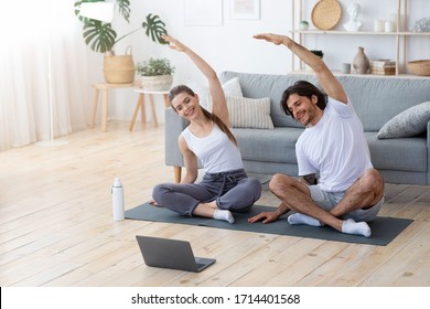 Healthy Couple Exercising At Home, Sitting On Sport Mat And Watching Videos On Laptop, Copy Space