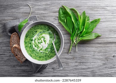 Healthy creamy soup with fresh ramson or wild garlic leaves on wooden background. Healthy spring food concept