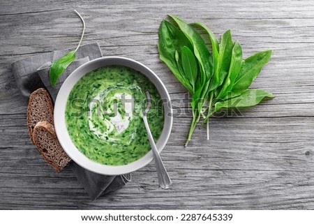 Healthy creamy soup with fresh ramson or wild garlic leaves on wooden background. Healthy spring food concept