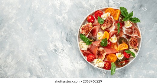 Healthy and delicious salad with mozzarella, figs, prosciutto, fresh basil leaves and tomato on a light background. Long banner format. top view. - Powered by Shutterstock