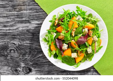 healthy delicious winter salad with persimmon slices, mix of spinach, arugula and lettuce leaves with blue cheese and walnuts on white plate on old dark wooden boards, view from above - Powered by Shutterstock