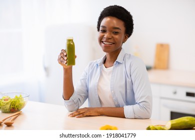 Healthy Detox. Black Woman Holding Smoothie Bottle Made Of Green Vegetables Posing In Modern Kitchen At Home, Smiling To Camera. Slimming And Weight Loss Diet Concept