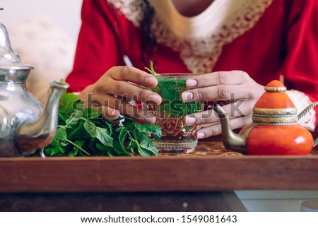 Healthy detox clear beverage. Close up of ethnic unrecognizable woman holding with hands green arab tea. Selective focus on the hot beverage. Arabian culture and traditions. Muslim lifestyle at home.