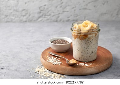 healthy diet breakfast. overnight oatmeal with chia seeds, bananas, peanut butter, honey in a glass jar on a gray concrete background